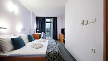 A hotel room with a bed, a desk, a television, and a balcony with curtains.