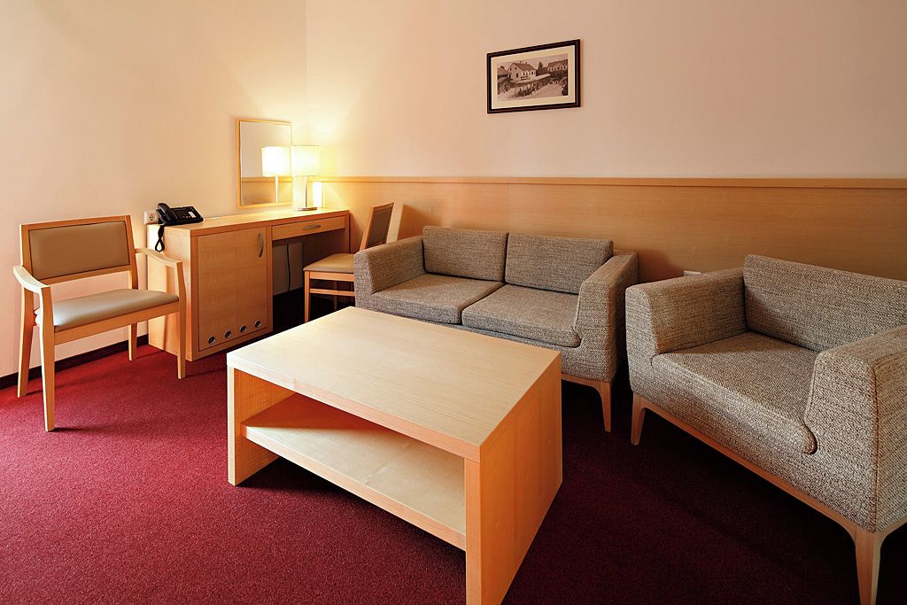 A hotel room with a wooden desk, two armchairs, a sofa, a small table, and a lamp.