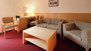 A hotel room with a wooden desk, two armchairs, a sofa, a small table, and a lamp.