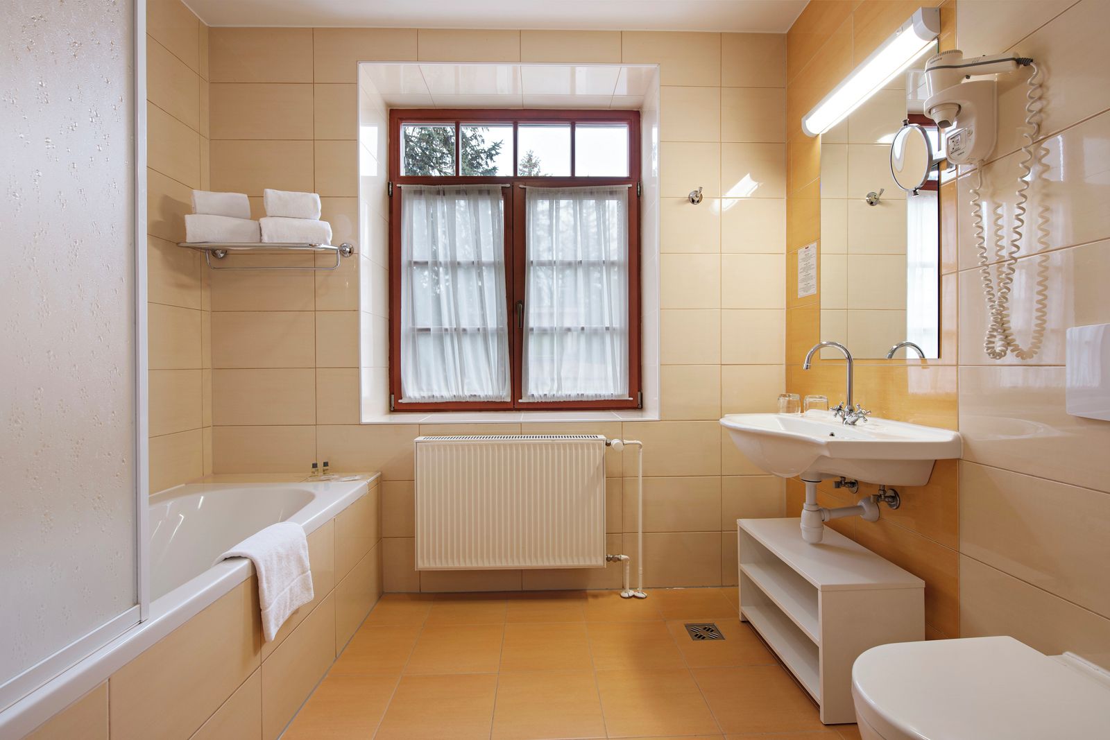 Een badkamer met een bad, een wastafel, een toilet, een raam met gordijnen en een radiator.