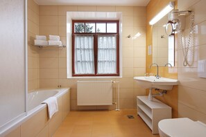Un baño con bañera, lavamanos, inodoro, ventana con cortinas y radiador.