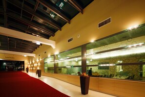 A hotel lobby with a red carpet, large windows with circular patterns, and a ceiling with exposed beams. - Izvir (Radenci)