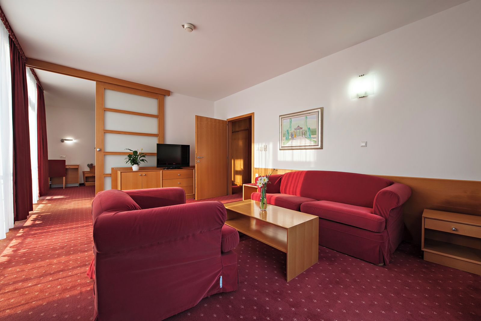 A living room with a red sofa, a wooden coffee table, and a TV on a wooden cabinet.