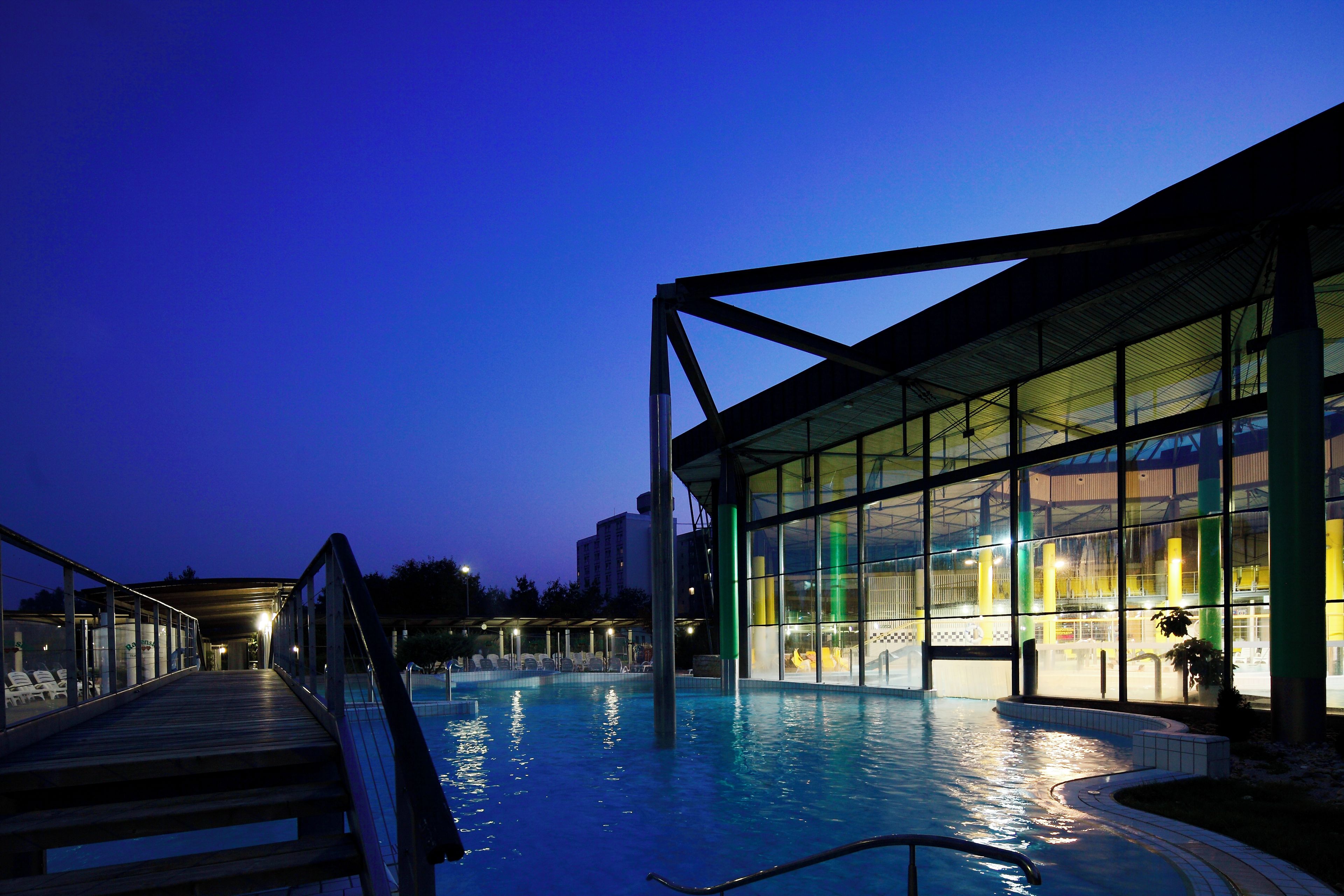An indoor swimming pool with a glass enclosure, a wooden deck, and a metal structure.
