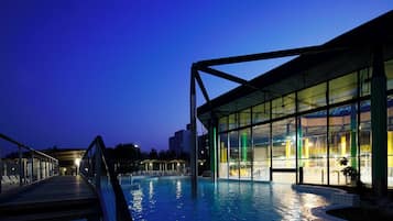 An indoor swimming pool with a glass enclosure, a wooden deck, and a metal structure.