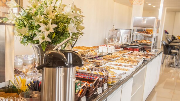 A buffet with a variety of food items, a coffee station, and a decorative white flower arrangement. - San Lucas Hotel (Sarandi)
