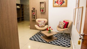 A modern living room with two armchairs, a coffee table, and a patterned rug. There are shelves with decorative items and a painting on the wall. - San Lucas Hotel (Sarandi)