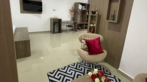 A modern living room with a sofa, a coffee table with flowers, a TV mounted on the wall, and a bookshelf. - San Lucas Hotel (Sarandi)