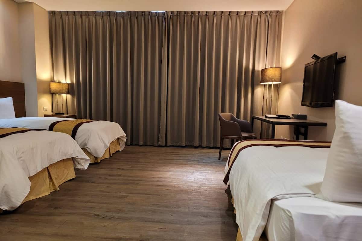 A hotel room with two beds, a desk, a chair, and a TV.