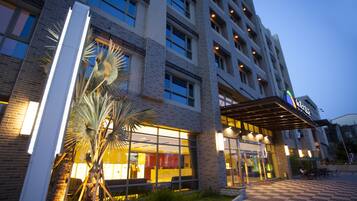 Welcome to our hotel, featuring a striking glass facade and inviting outdoor seating area.
