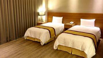 Habitación de hotel con dos camas, cabecero de madera, mesita de noche con lámpara y teléfono.