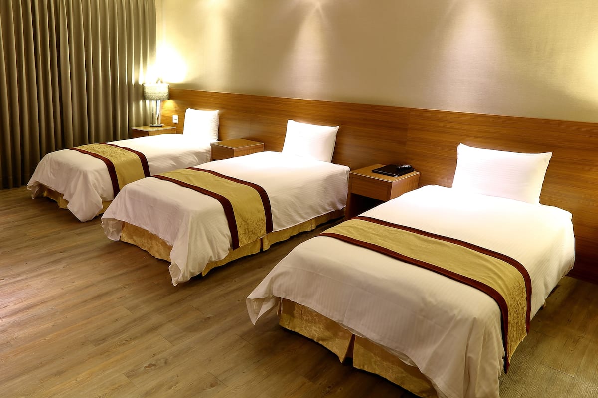 A hotel room with three beds, wooden headboards, and a nightstand with a lamp.