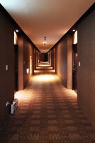Un largo y estrecho pasillo de hotel con suelos alfombrados y paredes iluminadas por luces del techo.