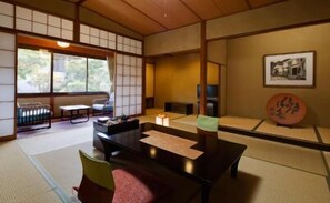 A traditional Japanese room with tatami flooring, a low table with cushions, a sliding door, and a framed picture on the wall.