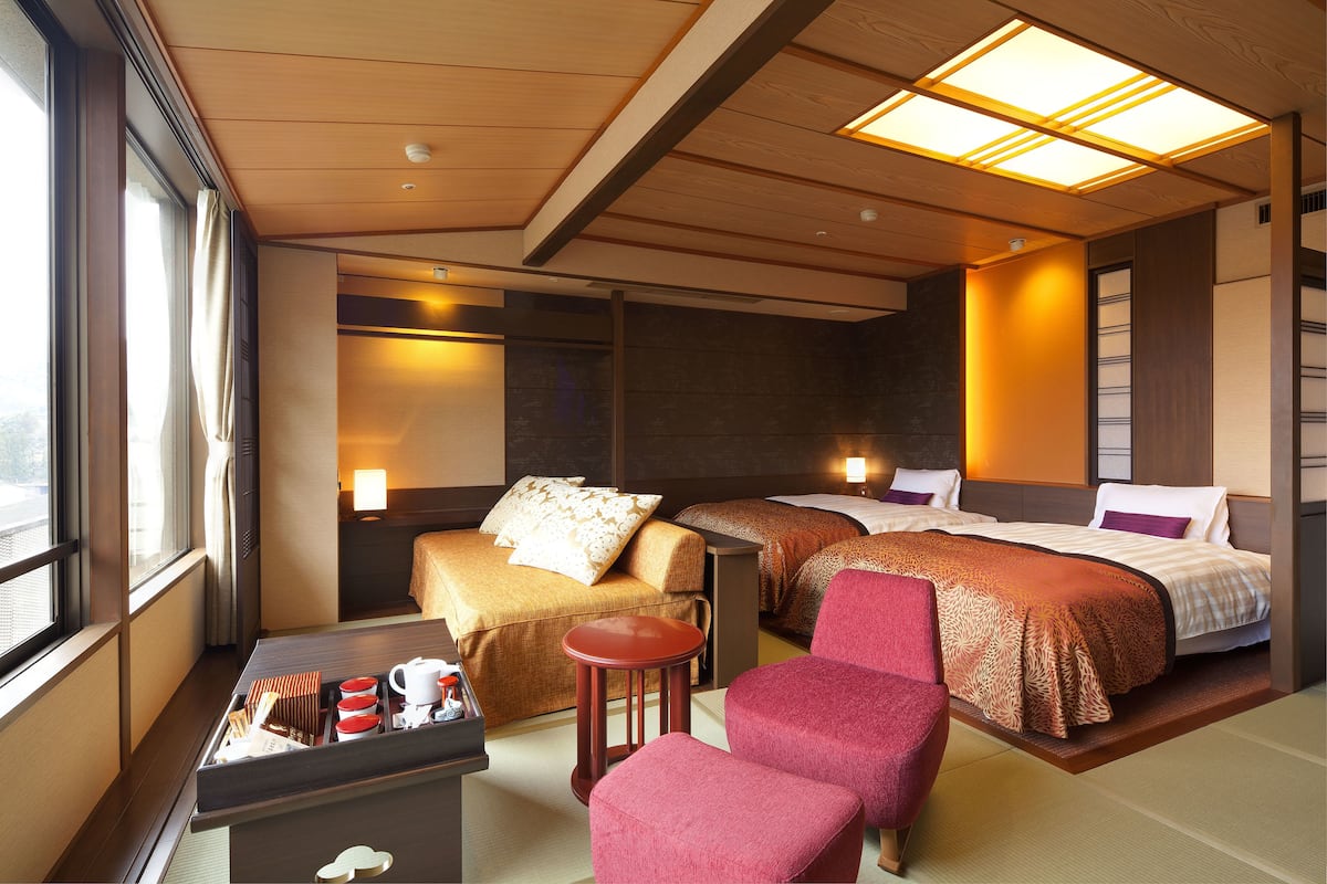 Une chambre d’hôtel avec deux lits, un coin salon avec une table et des chaises, et une fenêtre donnant sur un paysage.