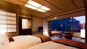 A hotel room with two beds, a desk, a TV, and a large window offering a view of the outdoors. - Kasuien Minami (Matsue)