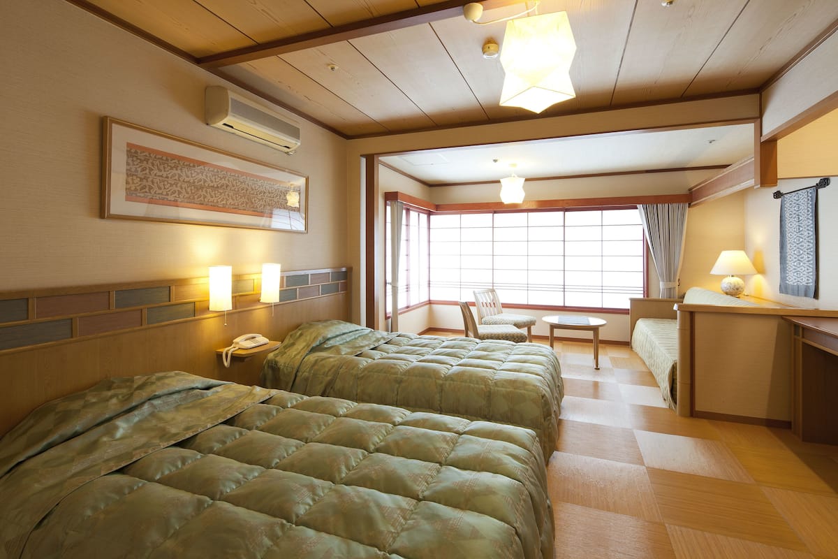 Une chambre d’hôtel avec deux lits, un bureau, une chaise et une fenêtre avec des rideaux.