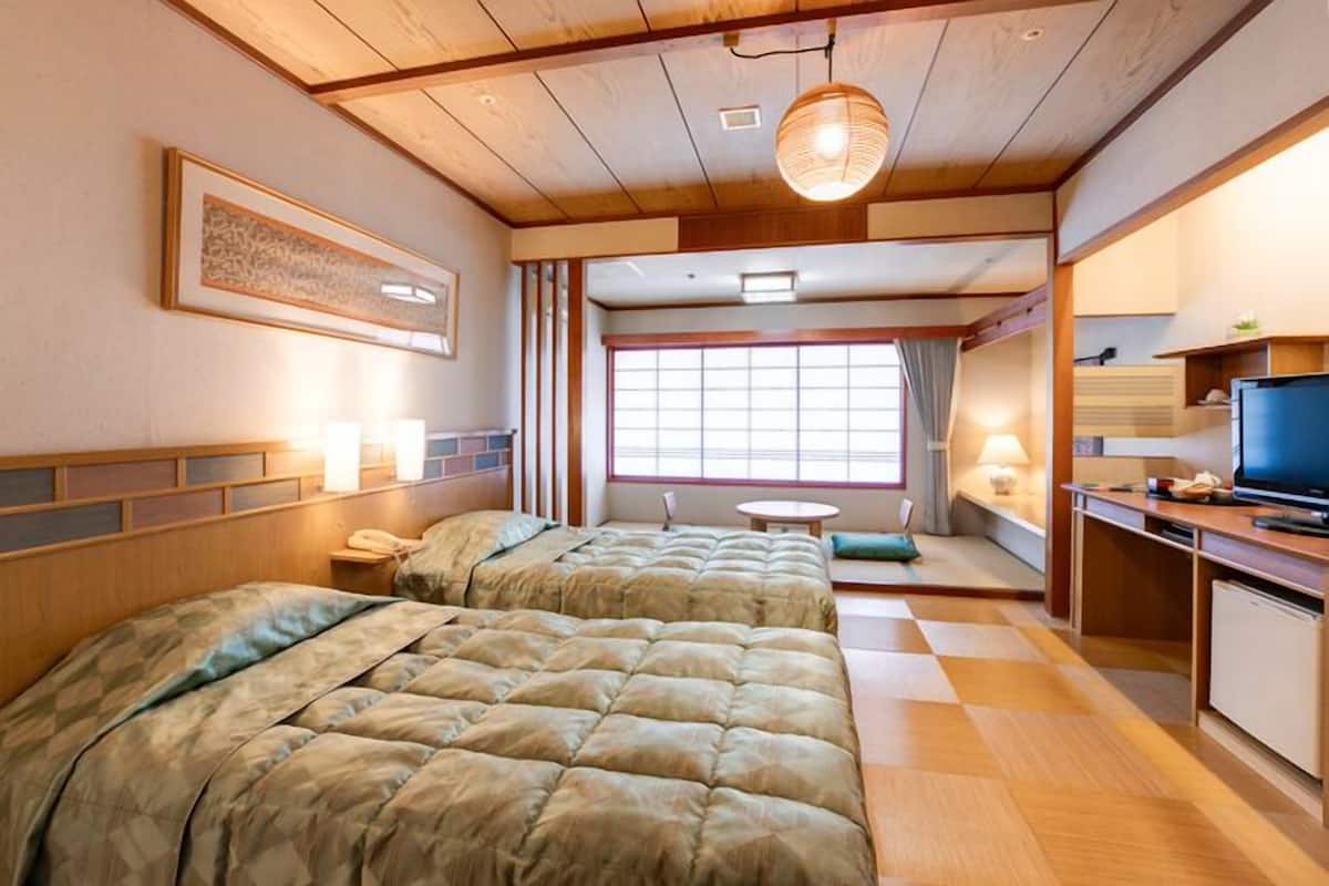 Une chambre d’hôtel avec deux lits, un bureau, une tél évision et une fenêtre avec des rideaux.