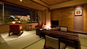 A modern living room with a wooden ceiling, a TV, a sofa, and a red chair. - Kasuien Minami (Matsue)