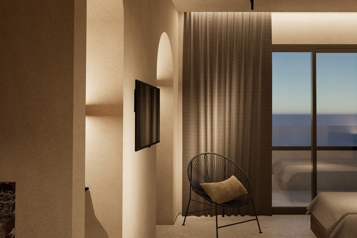 A bedroom with a bed, a chair, a large window, and a wall-mounted TV.