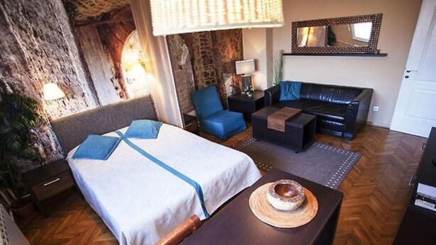 A hotel room with a bed, a sofa, a small table, and a mirror. - Studio Orient (Belgrade)