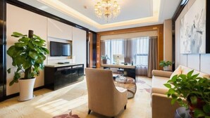 A modern living room with a flat-screen TV, a sofa, a chair, and a coffee table. There are potted plants and a chandelier. - New Century Grand Hotel Siyang (Suqian)