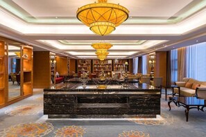A lobby with a central marble reception desk, bookshelves, and a chandelier.