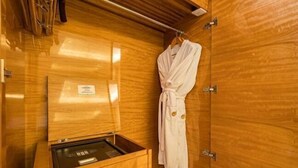 A wooden room with a wooden cabinet containing a small appliance, a robe hanging on the wall, and a wooden door. - New Century Grand Hotel Siyang (Suqian)