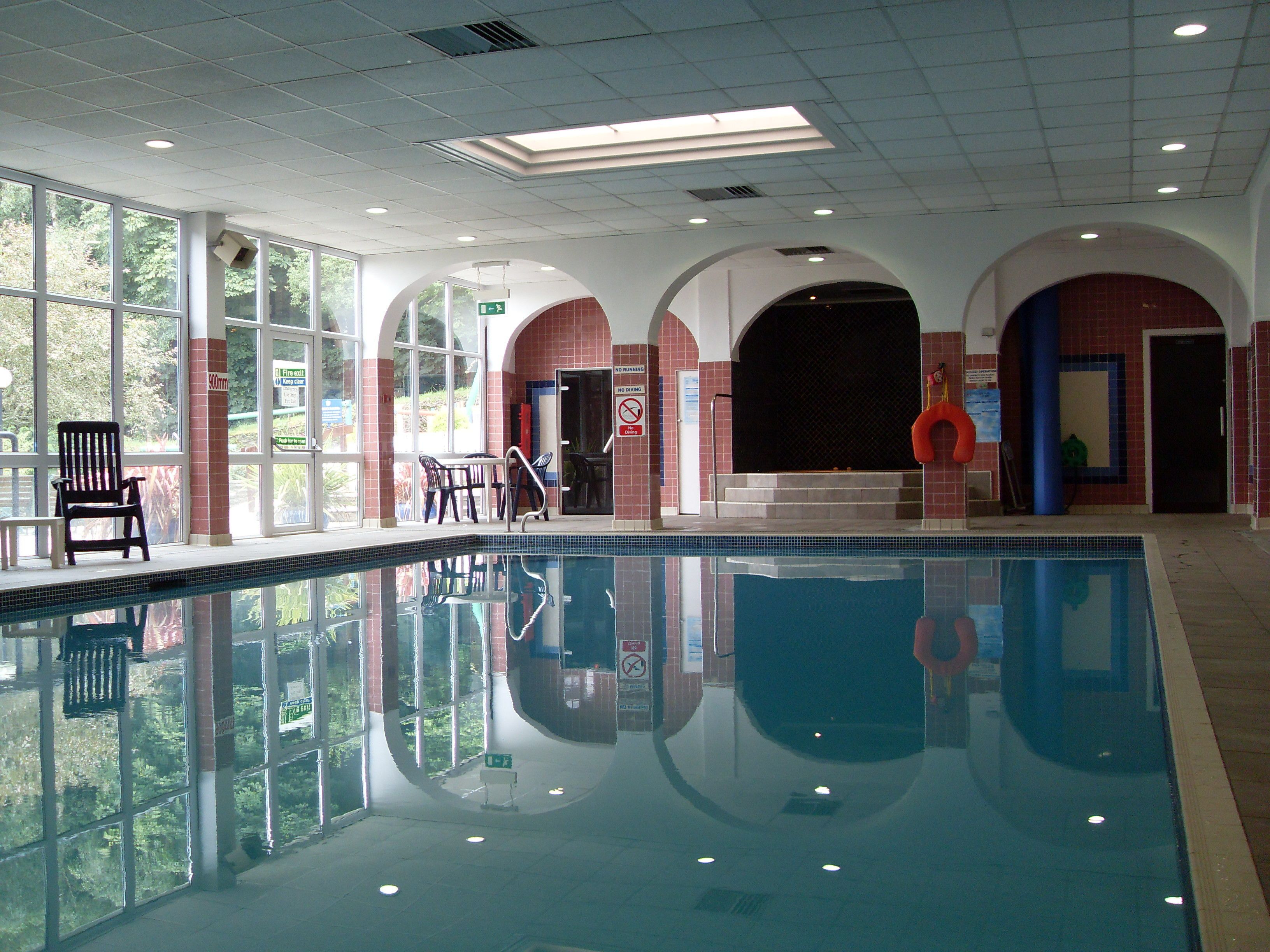 An indoor swimming pool with clear glass walls, a black chair, and a lifebuoy.