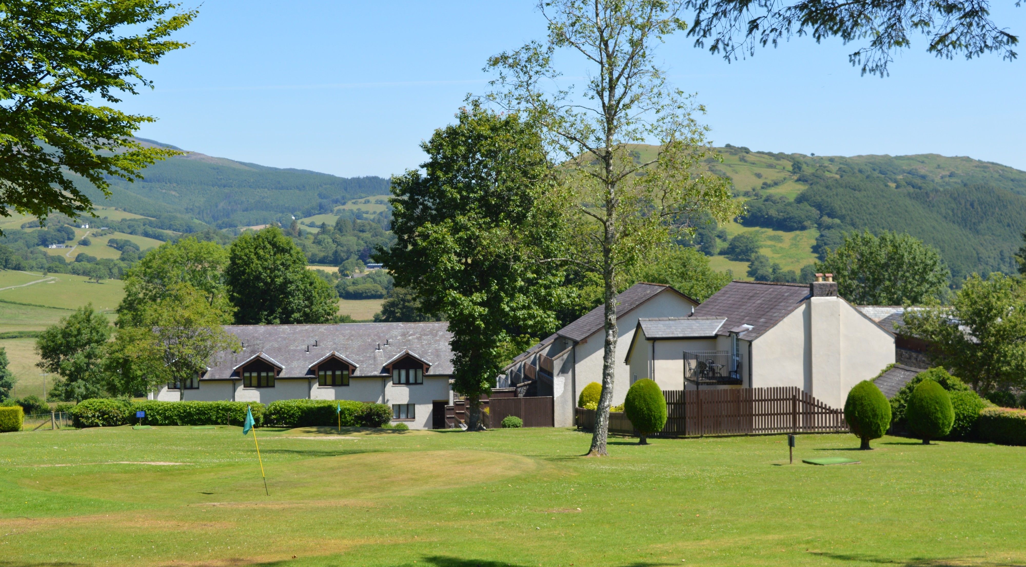 A traditional building with multiple gabled roofs, surrounded by a well-maintained lawn and mature trees.