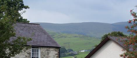 A stone building with a pitched roof and a white building with a flat roof in the background.