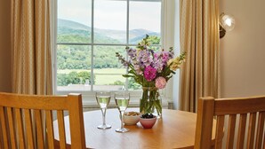 A wooden table with two glasses of white wine, a bowl of almonds, a bowl of olives, and a vase of flowers.