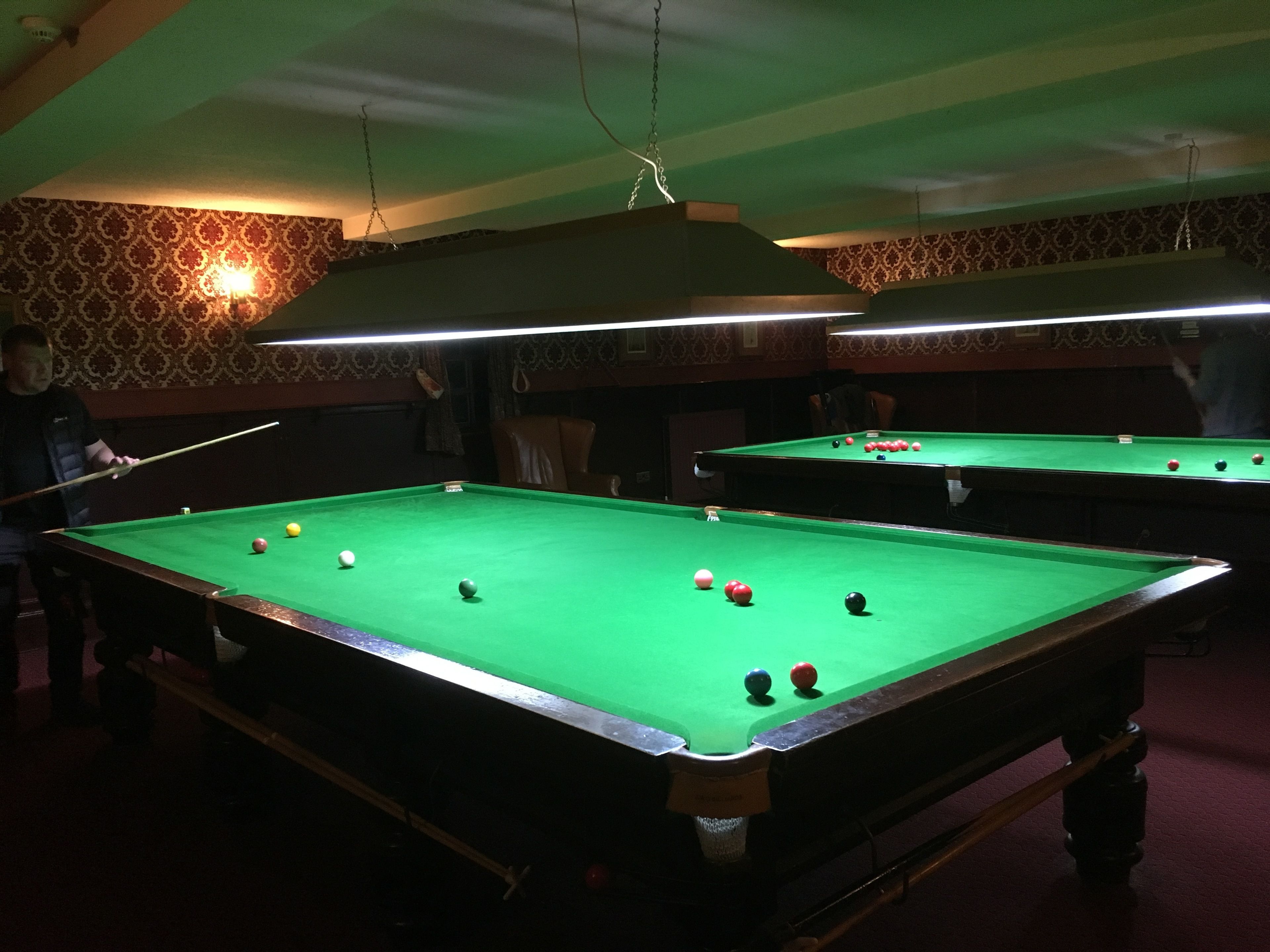 A pool table with balls, a chair, and a person playing.