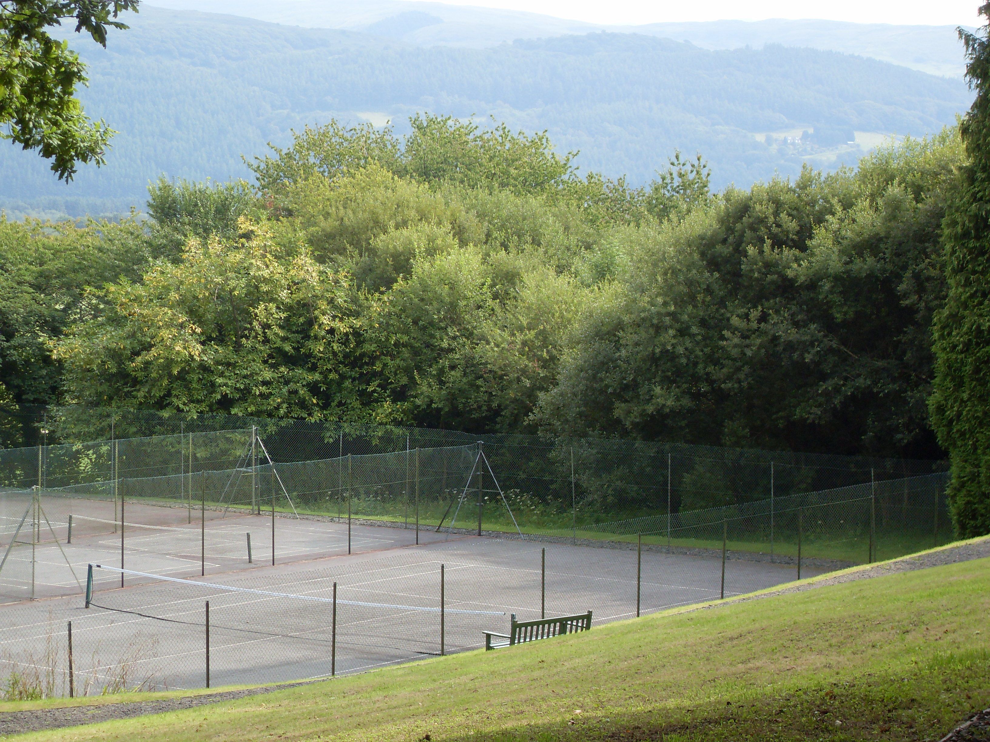En tennisbana omgiven av träd och kullar.