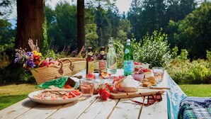 A picnic setup with a table, food, drinks, and a basket of flowers.