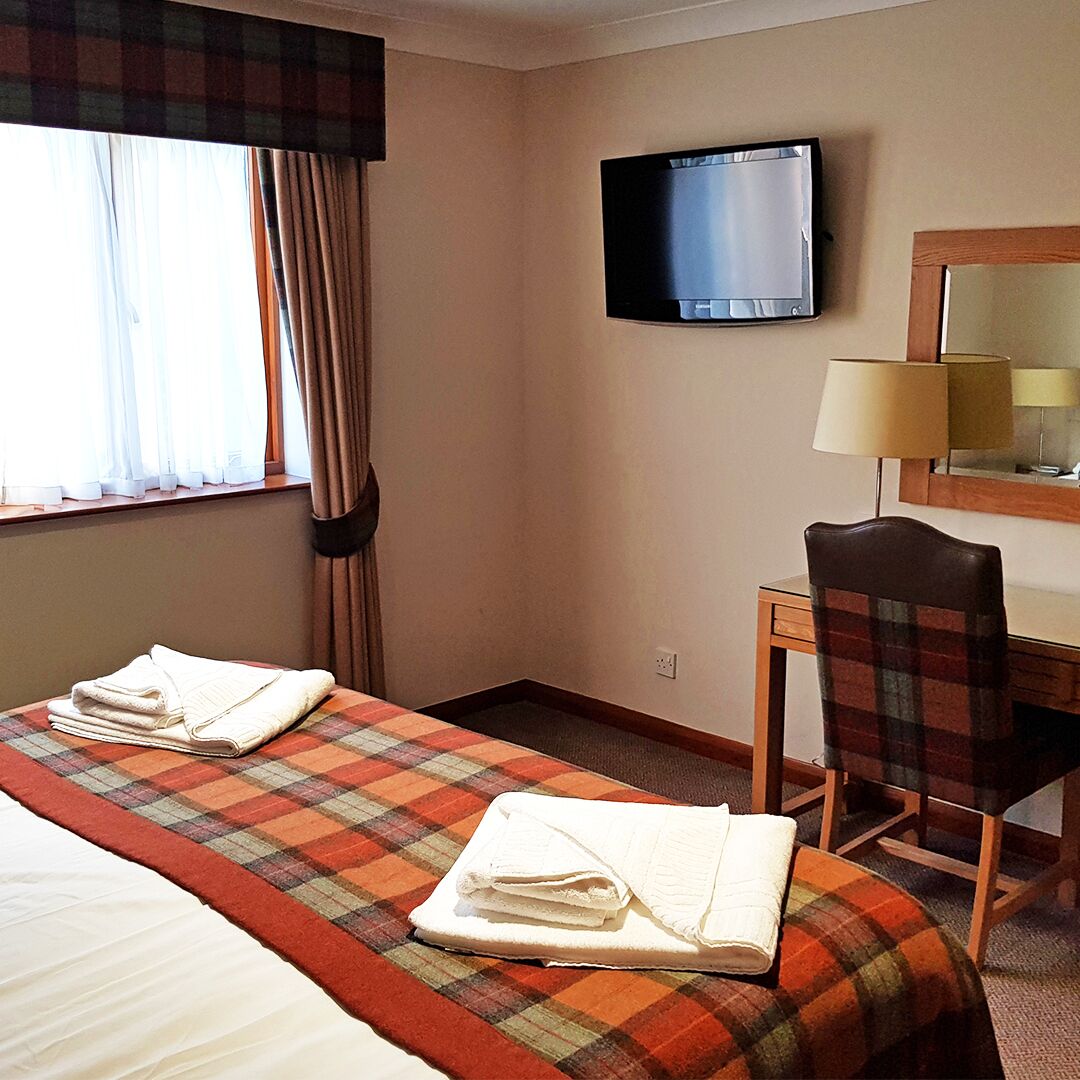 Une chambre d’hôtel équipée d’un lit, d’un bureau, d’une chaise, d’une télévision et d’une fenêtre avec des rideaux.