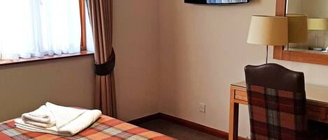 A hotel room with a bed, a desk, a chair, a television, and a window with curtains.