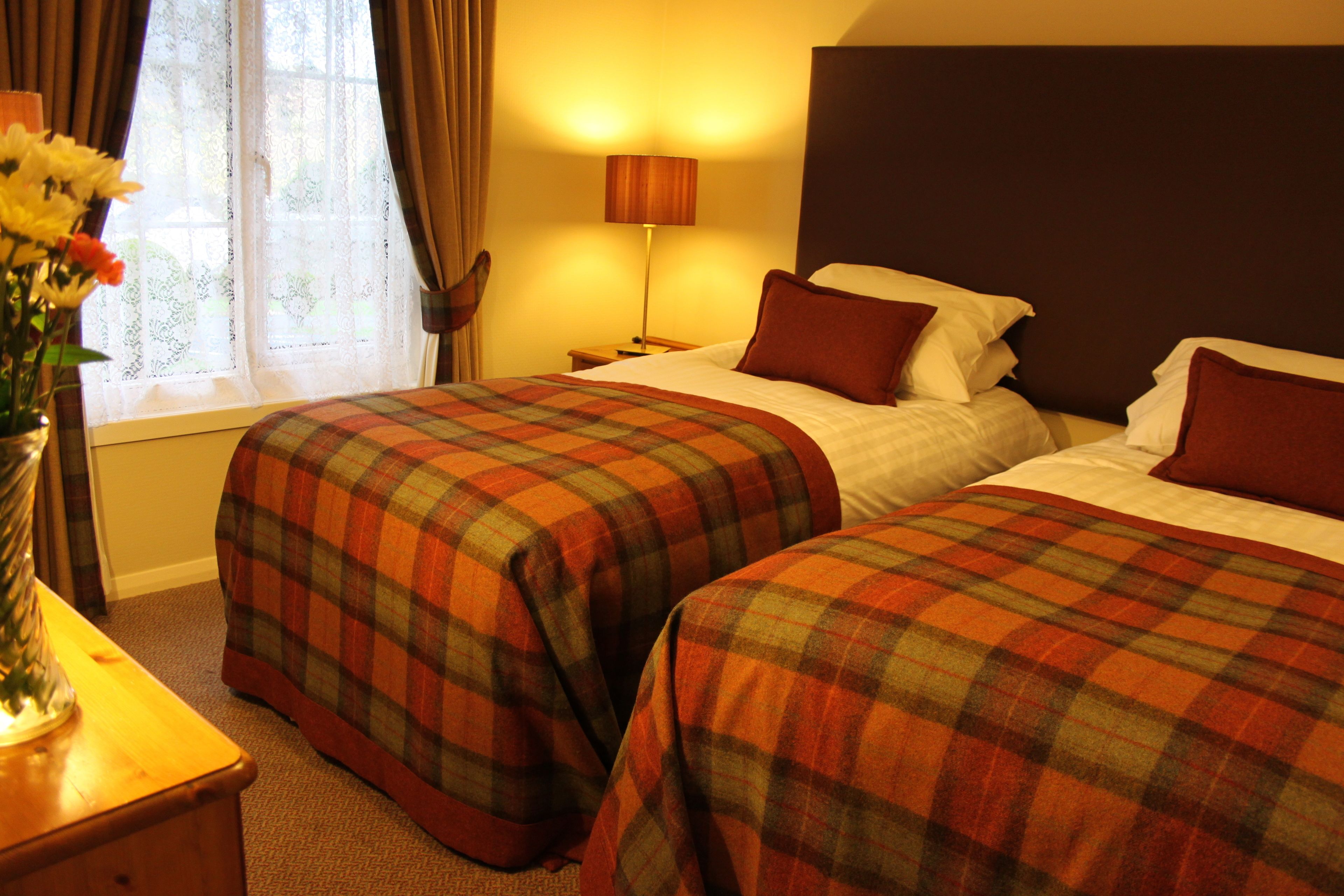 A hotel room with two beds, a nightstand, a lamp, and a window with curtains.