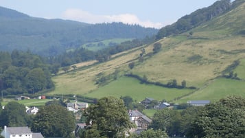 A rural landscape with rolling hills, scattered houses, and a mix of open fields and wooded areas.