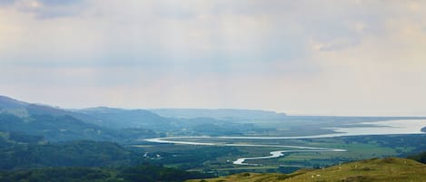 A panoramic view of a river winding through a valley with hills and a cloudy sky.