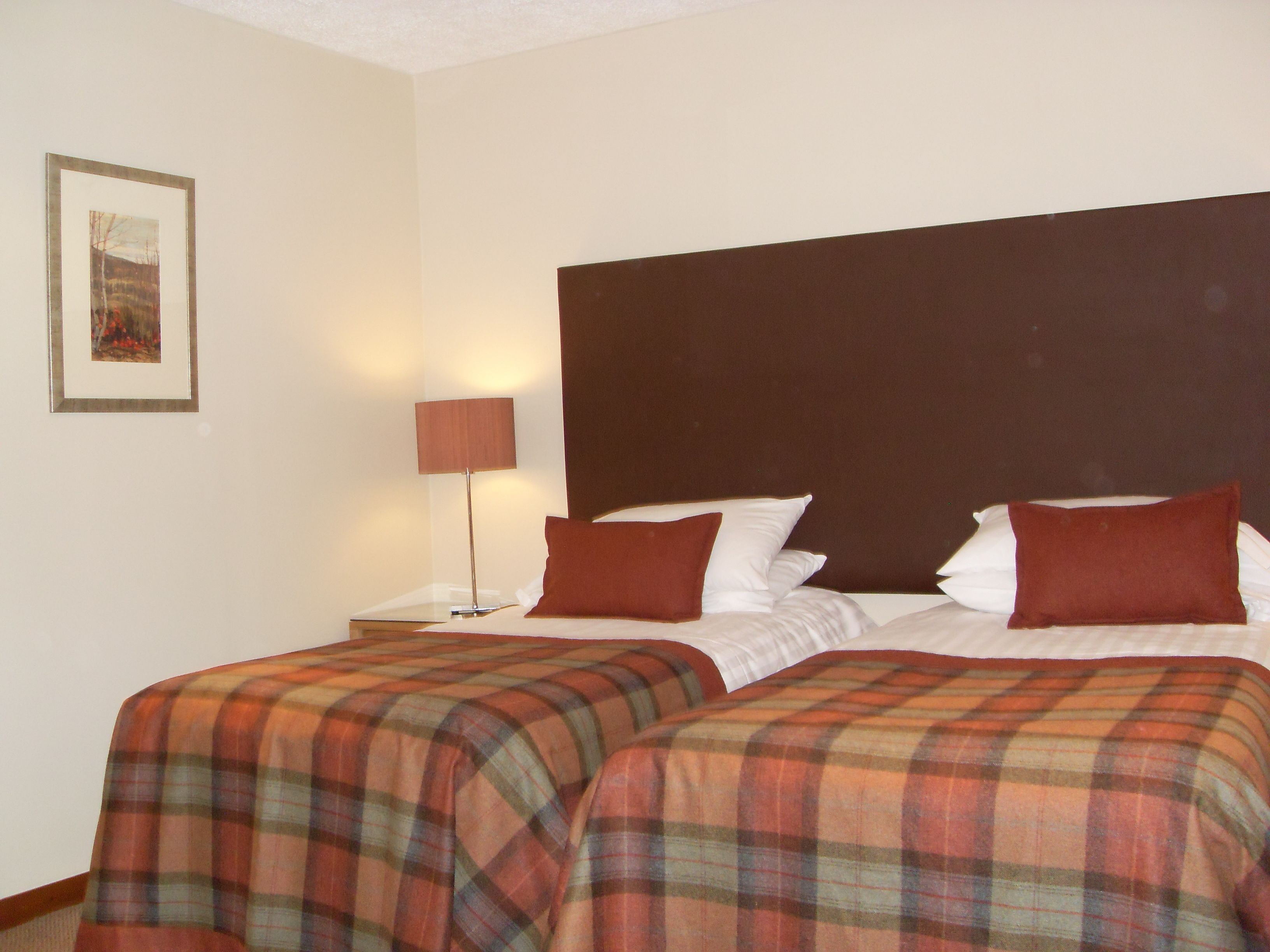 A hotel room with two beds, a nightstand, a lamp, and a framed picture on the wall.