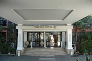 The entrance of a hotel with a covered entrance, steps leading up to it, and a sign above the doors. - Univers (Elbasan)