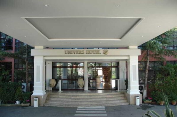 The entrance of a hotel with a covered entrance, steps leading up to it, and a sign above the doors. - Univers (Elbasan)
