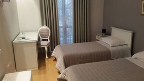 A hotel room with two beds, a desk, a chair, a nightstand, and a window with curtains. - Univers (Elbasan)