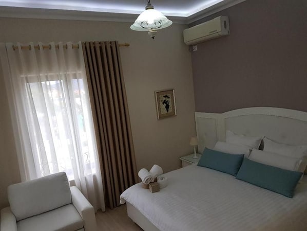 A hotel room with a bed, a chair, a nightstand, and a window with curtains. - Univers (Elbasan)