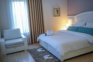 A hotel room with a bed, a chair, a window with curtains, and a wall-mounted picture. - Univers (Elbasan)