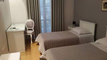 A hotel room with two beds, a desk, a chair, a nightstand, and a window with curtains.