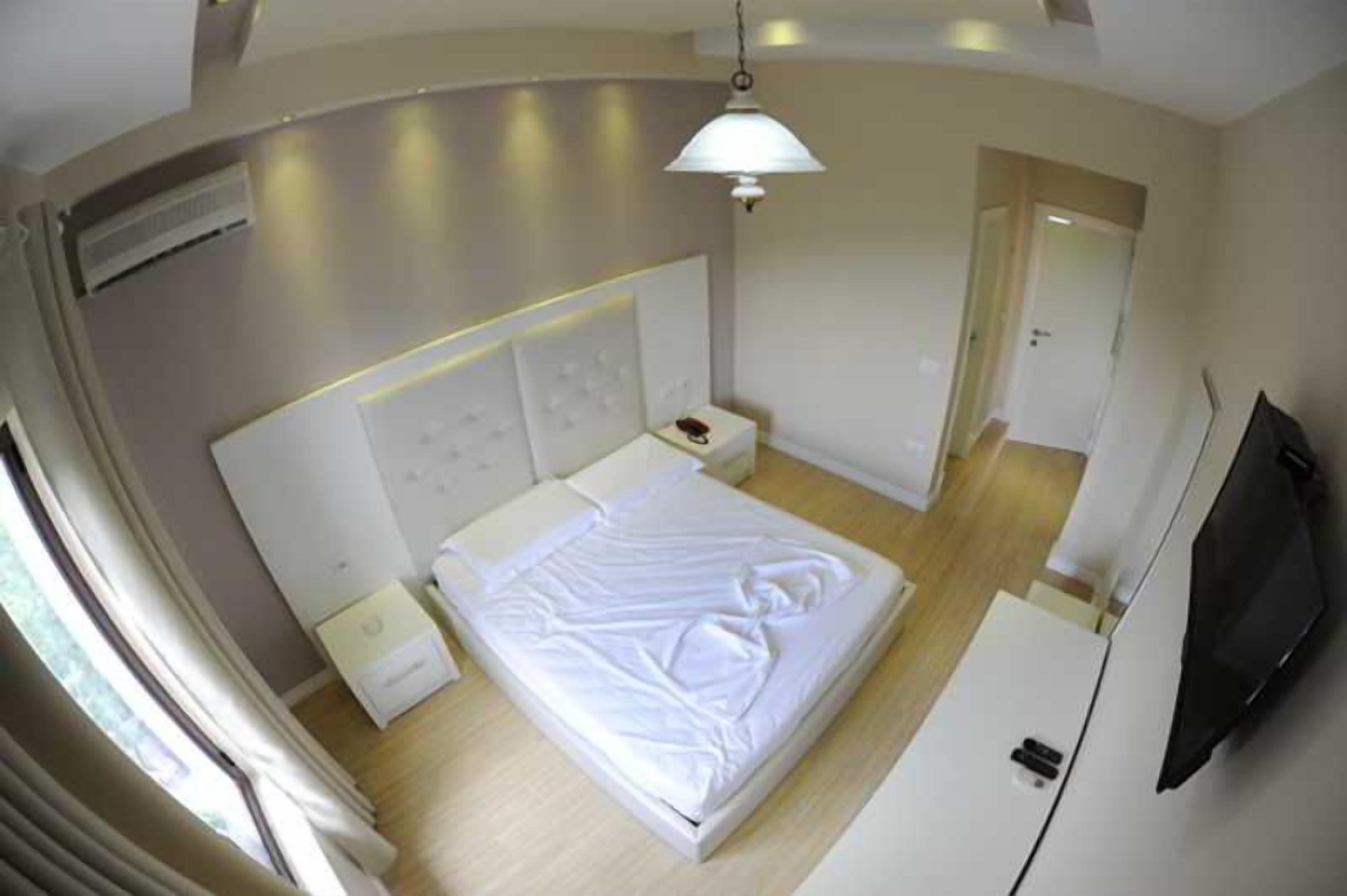 Ett hotellrum med en säng, sängbord, en platt-TV och en dörr som leder till ett annat rum.