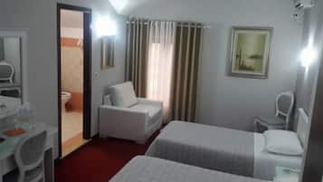 A hotel room with a bed, a chair, a desk with a mirror, and a window with curtains.