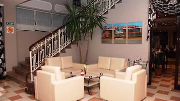 A hotel lobby with a staircase, a seating area with two sofas, a coffee table, and a potted plant.